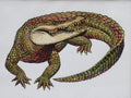 A green and gold crocodile with an open mouth and curled tail, on white paper.