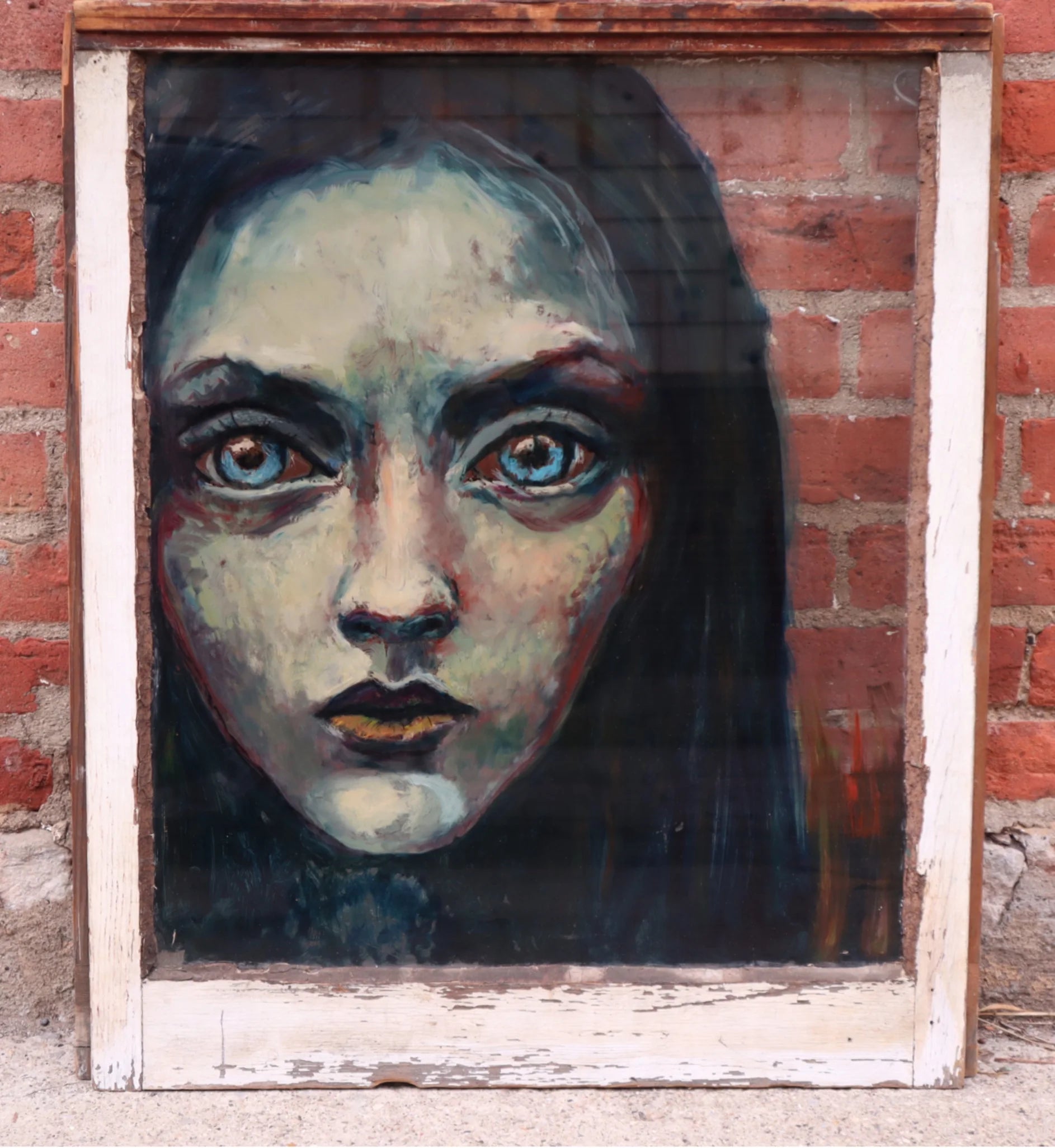 A pale, blue-toned portrait in a worn white frame against a brick wall.